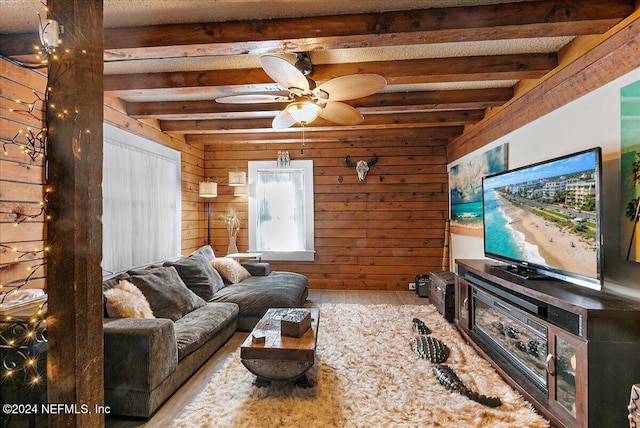 living room featuring a wealth of natural light, wooden walls, hardwood / wood-style flooring, beamed ceiling, and ceiling fan