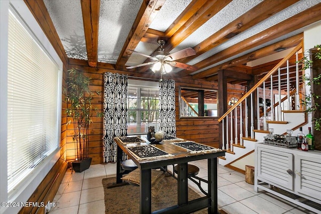 dining area with wood walls, beamed ceiling, ceiling fan, a textured ceiling, and light tile patterned floors