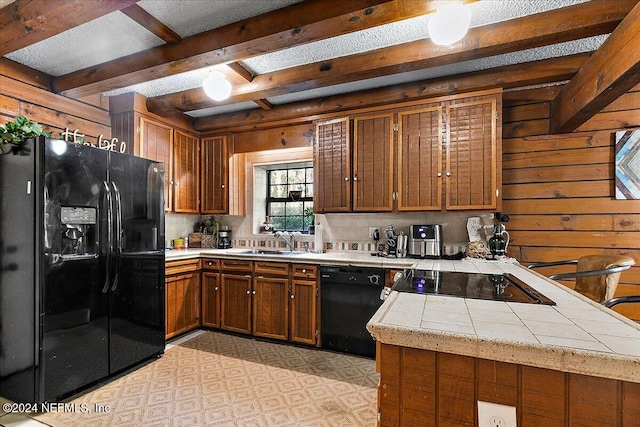 kitchen featuring black appliances, wooden walls, sink, beamed ceiling, and kitchen peninsula