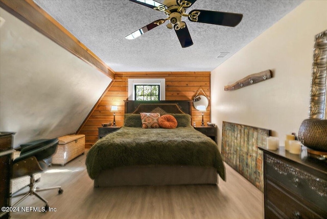 bedroom featuring wood walls, hardwood / wood-style floors, ceiling fan, and a textured ceiling