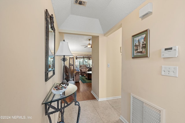 hallway featuring light tile patterned flooring, a textured ceiling, and a raised ceiling