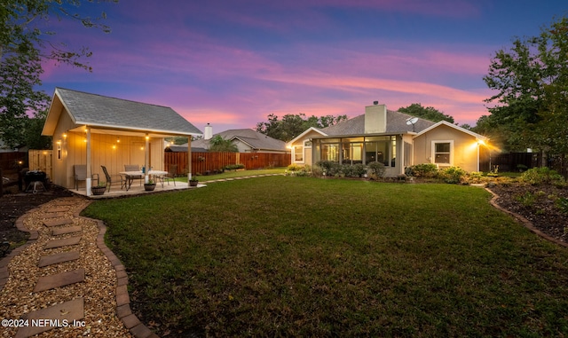 back house at dusk featuring a lawn, a patio, and a sunroom