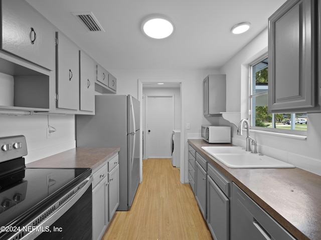 kitchen featuring washer / clothes dryer, light hardwood / wood-style flooring, sink, gray cabinets, and black range with electric stovetop