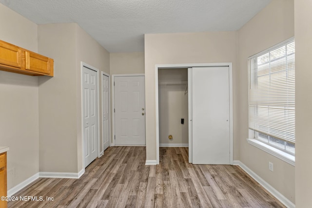 unfurnished bedroom with a textured ceiling, two closets, and light wood-type flooring