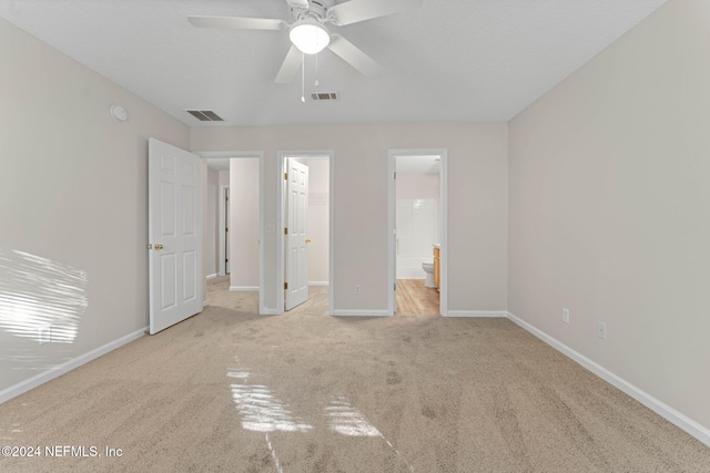 unfurnished bedroom with a spacious closet, ensuite bath, a closet, light carpet, and ceiling fan