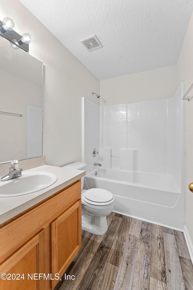 full bathroom featuring a textured ceiling, hardwood / wood-style flooring, toilet, vanity, and shower / bath combination