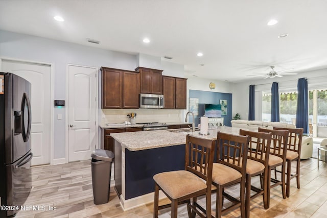 kitchen with light hardwood / wood-style flooring, an island with sink, sink, a kitchen bar, and appliances with stainless steel finishes