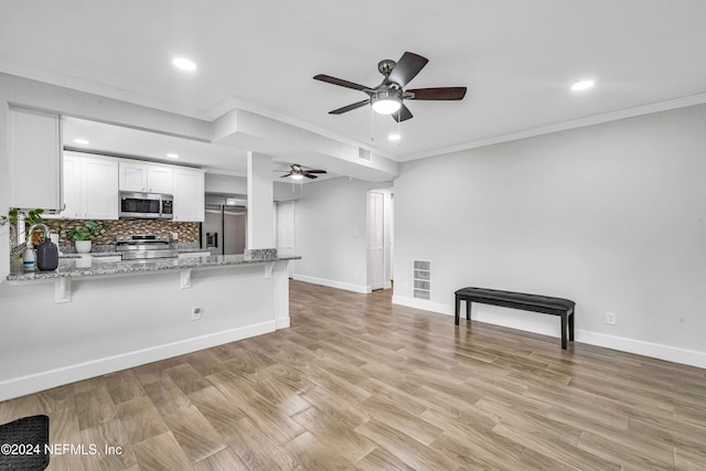 unfurnished living room with ceiling fan, ornamental molding, and light wood-type flooring