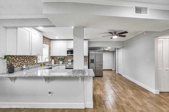 kitchen featuring kitchen peninsula, light wood-type flooring, ornamental molding, appliances with stainless steel finishes, and white cabinetry