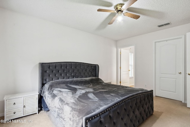 bedroom with ceiling fan, a textured ceiling, ensuite bathroom, and light colored carpet