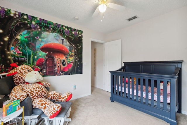 bedroom featuring a nursery area, a textured ceiling, carpet flooring, and ceiling fan