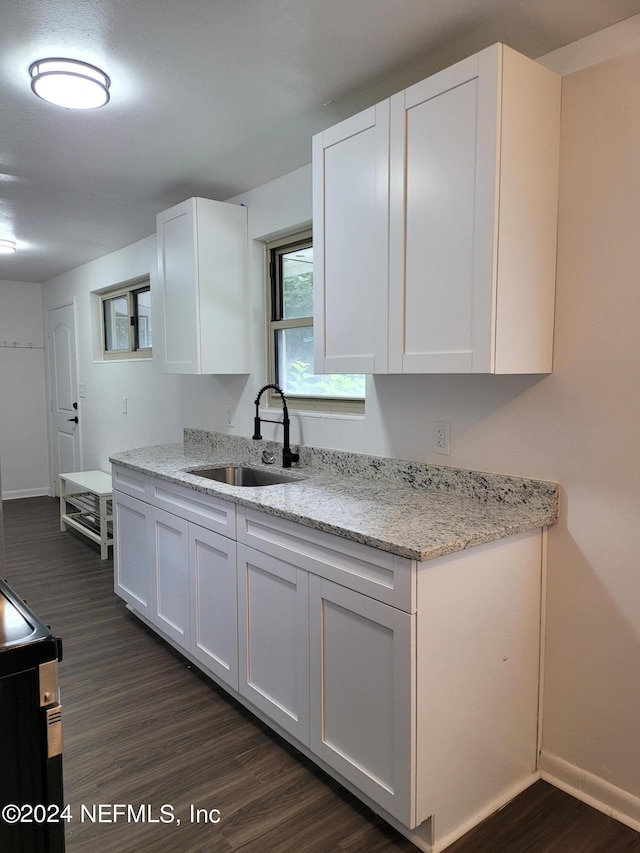 kitchen with light stone countertops, sink, stove, white cabinets, and dark wood-type flooring