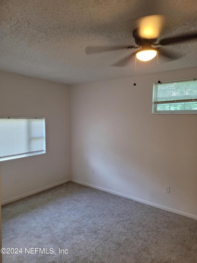 carpeted empty room featuring a textured ceiling, plenty of natural light, and ceiling fan