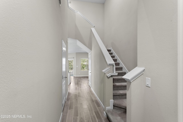 hallway with a towering ceiling, wood finish floors, stairway, and baseboards