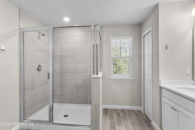 bathroom with a shower stall, wood tiled floor, baseboards, and vanity