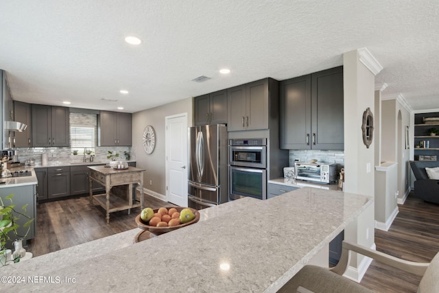 kitchen featuring sink, a textured ceiling, stainless steel appliances, dark wood-type flooring, and ornamental molding