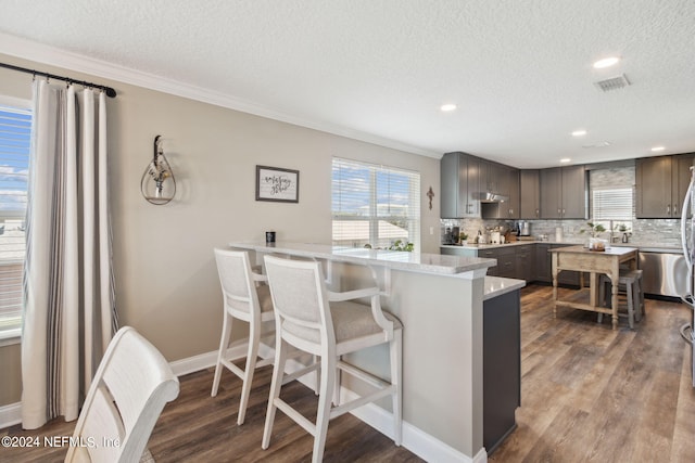 kitchen featuring decorative backsplash, a kitchen breakfast bar, a textured ceiling, dark wood-type flooring, and crown molding