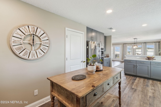 kitchen with a textured ceiling, gray cabinetry, pendant lighting, and wood-type flooring