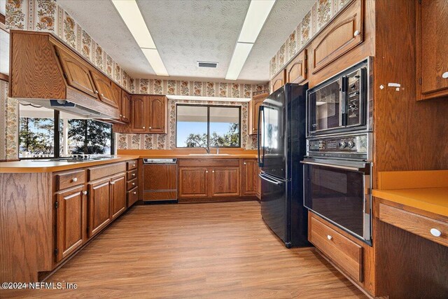 kitchen featuring a textured ceiling, sink, light hardwood / wood-style flooring, and black appliances