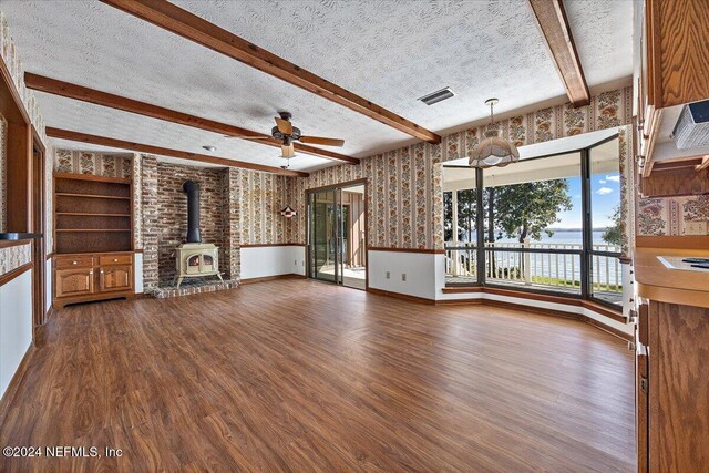 unfurnished living room featuring hardwood / wood-style floors, a wood stove, ceiling fan, a textured ceiling, and beamed ceiling