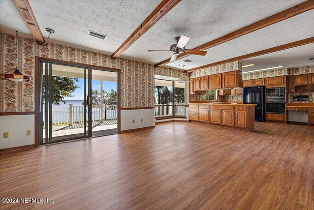 kitchen with beam ceiling, hardwood / wood-style floors, black appliances, and a textured ceiling