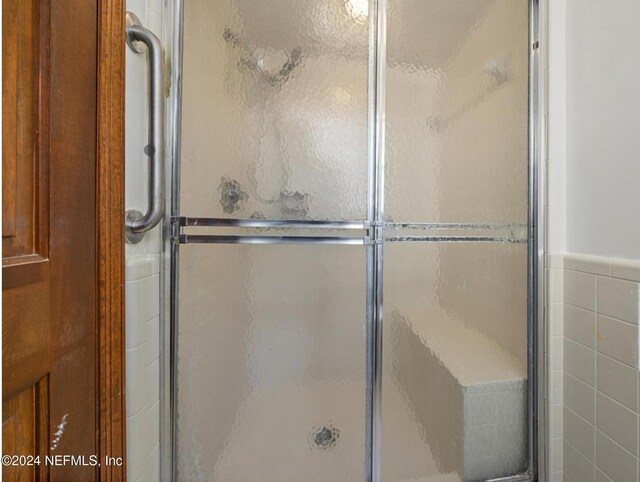 bathroom featuring a shower with shower door and tile walls