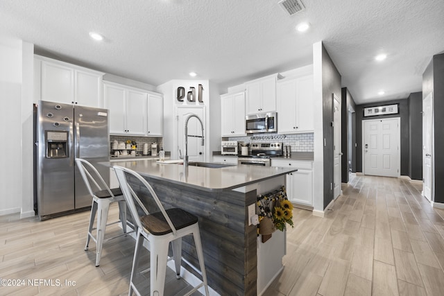 kitchen with an island with sink, stainless steel appliances, a kitchen bar, white cabinetry, and a textured ceiling