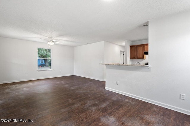 unfurnished living room featuring ceiling fan, a textured ceiling, and dark hardwood / wood-style flooring