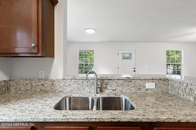 kitchen featuring a textured ceiling, light stone countertops, sink, and plenty of natural light