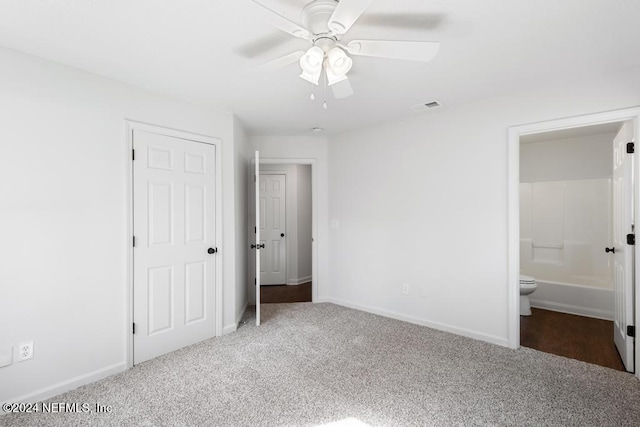 unfurnished bedroom with dark colored carpet, ensuite bathroom, and ceiling fan