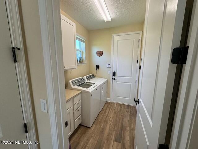 washroom featuring a textured ceiling, light wood-type flooring, cabinets, and washer and clothes dryer