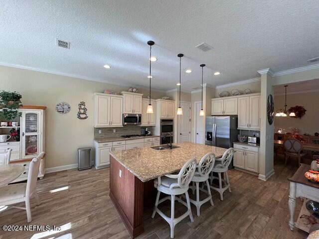 kitchen featuring a textured ceiling, stainless steel appliances, an island with sink, sink, and a breakfast bar area