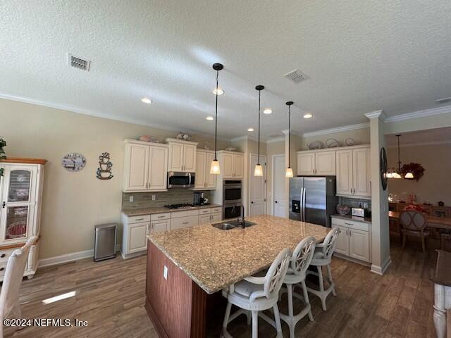 kitchen with a textured ceiling, decorative backsplash, an island with sink, stainless steel appliances, and a breakfast bar area