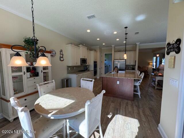 dining space featuring sink, dark wood-type flooring, a textured ceiling, a notable chandelier, and ornamental molding