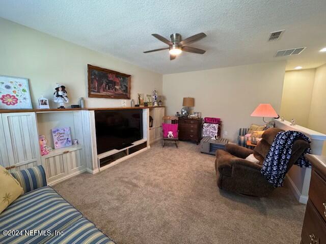 living room with ceiling fan, light colored carpet, and a textured ceiling