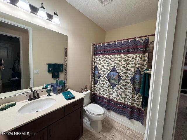 full bathroom featuring a textured ceiling, tile patterned flooring, vanity, toilet, and shower / bath combo with shower curtain