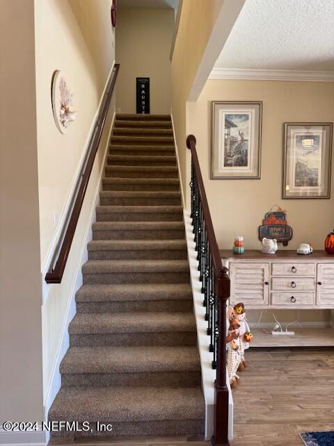 stairway featuring hardwood / wood-style floors, a textured ceiling, and ornamental molding