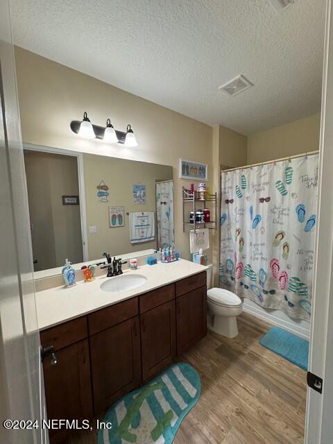 full bathroom with a textured ceiling, vanity, shower / bath combination with curtain, toilet, and hardwood / wood-style flooring