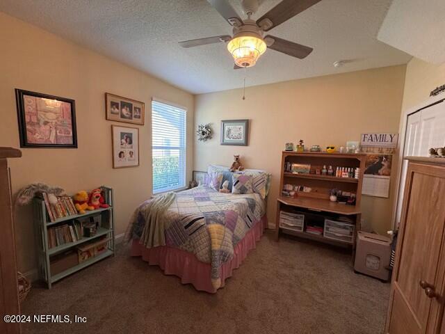 bedroom featuring ceiling fan, dark carpet, and a textured ceiling