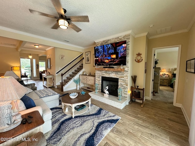 living room with light hardwood / wood-style flooring, ceiling fan, a fireplace, a textured ceiling, and ornamental molding