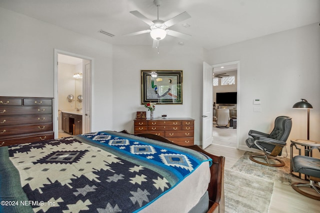 bedroom with light wood-type flooring, ceiling fan, and connected bathroom