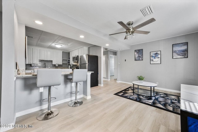 kitchen with kitchen peninsula, white cabinets, appliances with stainless steel finishes, a kitchen bar, and light hardwood / wood-style flooring