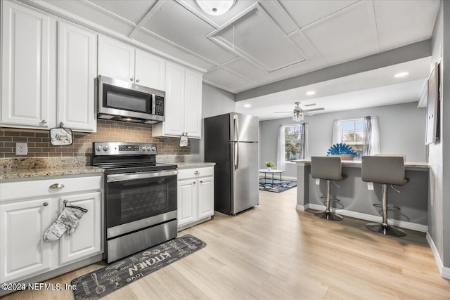 kitchen with light stone counters, appliances with stainless steel finishes, light hardwood / wood-style flooring, and white cabinetry