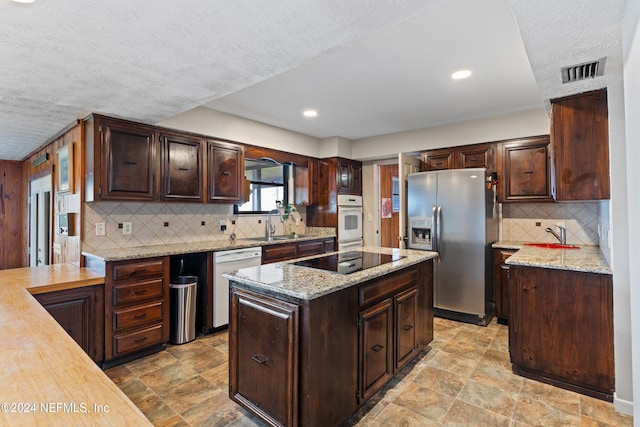 kitchen with dark brown cabinetry, white appliances, a textured ceiling, and a kitchen island