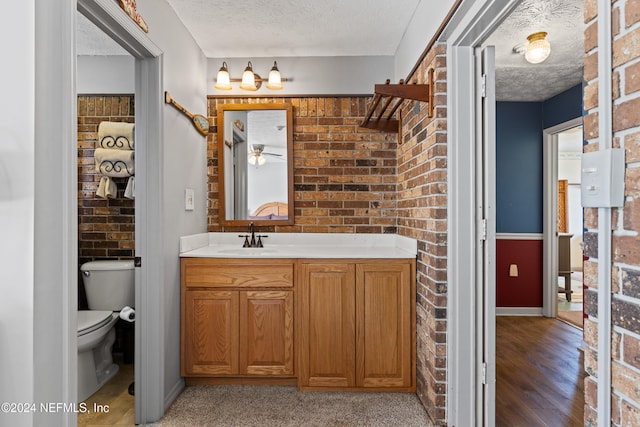 bathroom featuring vanity, a textured ceiling, hardwood / wood-style floors, toilet, and brick wall