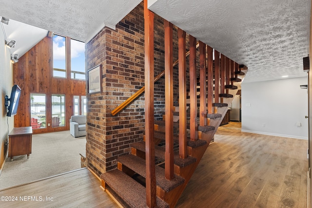 staircase with hardwood / wood-style floors, wood walls, a textured ceiling, and high vaulted ceiling