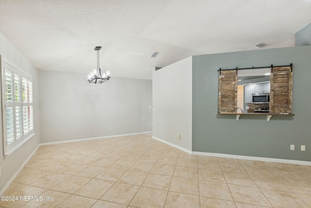 tiled spare room featuring a textured ceiling, a chandelier, and a barn door