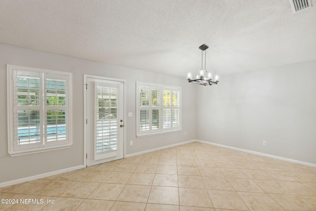 tiled spare room featuring an inviting chandelier, a textured ceiling, and plenty of natural light