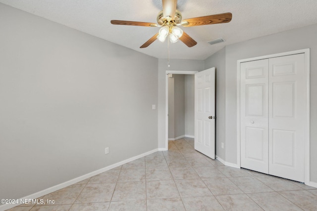 unfurnished bedroom featuring a closet, a textured ceiling, light tile patterned floors, and ceiling fan