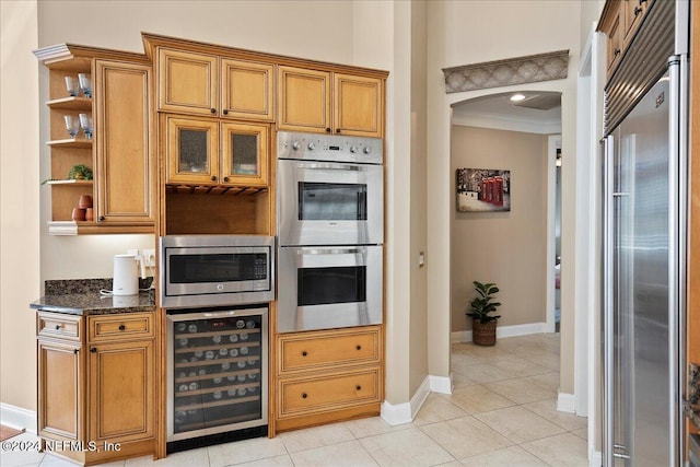 kitchen featuring beverage cooler, built in appliances, dark stone countertops, light tile patterned floors, and ornamental molding